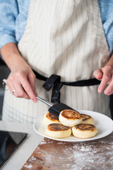 Hands of a female chef placing freshly cooked syrniki on a plate, garnishing with sour cream and mint. Concept of home cooking, traditional recipes, and culinary presentation.