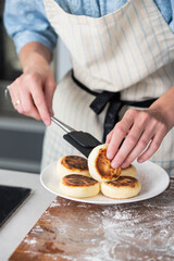 Hands of a female chef placing freshly cooked syrniki on a plate, garnishing with sour cream and mint. Concept of home cooking, traditional recipes, and culinary presentation.