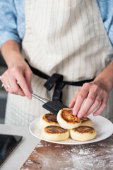 Hands of a female chef placing freshly cooked syrniki on a plate, garnishing with sour cream and mint. Concept of home cooking, traditional recipes, and culinary presentation.