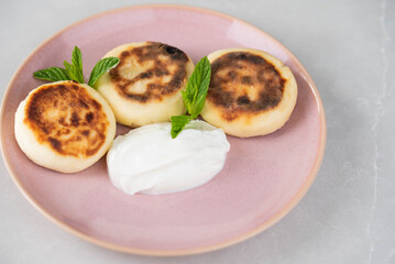 Syrniki (cottage cheese pancakes) on a plate, garnished with sour cream and mint, ready to be enjoyed for breakfast. Concept of home cooking, traditional recipes, and delicious morning meals.