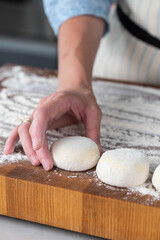 Hands of a female chef preparing homemade syrniki (cottage cheese pancakes)  by coating them in flour on a wooden board before frying. Home cooking, traditional recipes, and culinary preparation.