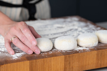 Hands of a female chef preparing homemade syrniki (cottage cheese pancakes)  by coating them in flour on a wooden board before frying. Home cooking, traditional recipes, and culinary preparation.