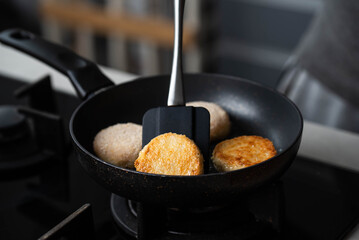 Meatballs or small meat patties cutlets sizzling in oil while frying in a pan on the stove. Concept of home cooking, traditional recipes, and culinary preparation