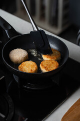 Meatballs or small meat patties cutlets sizzling in oil while frying in a pan on the stove. Concept of home cooking, traditional recipes, and culinary preparation