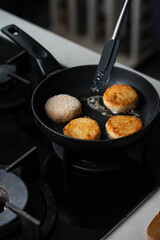 Meatballs or small meat patties cutlets sizzling in oil while frying in a pan on the stove. Concept of home cooking, traditional recipes, and culinary preparation