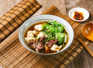 Beef dumplings soup with meat, chilli sauce, spring onion, wooden spoon, and chopsticks served in...