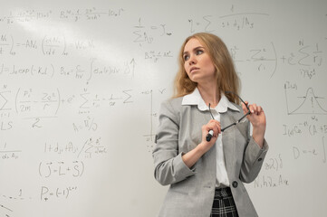 A Caucasian woman stands at a blackboard with written formulas.