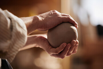 Side view closeup of senior woman carefully holding clay ball in hands and creating handmade...