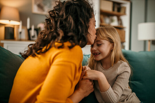 Loving mother and her daughter sitting on the couch, holding hands and sharing their stories. Mother and daughter bonding concept