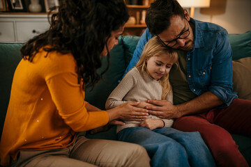 Naklejka premium Worried father and mother consoling their little girl who is having stomachache at home