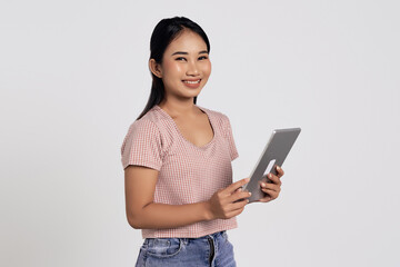 Smiling happy fun young Asian woman in a casual t-shirt holding digital tablet pc computer and...