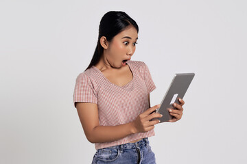 Surprised beautiful young Asian woman in a casual t-shirt using digital tablet pc computer, reading good news isolated on white background