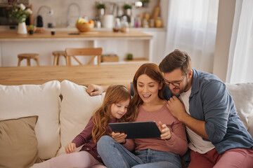 Curious little girl using the tablet with her parents in the living room