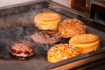 A hamburger being assembled and served, with fresh ingredients layered onto a juicy patty and a toasted bun.