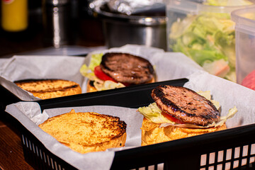 A hamburger being assembled and served, with fresh ingredients layered onto a juicy patty and a toasted bun.