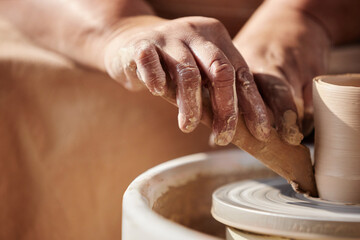 Detail shot of female hands carefully shaping clay on pottery wheel in sunlight copy space