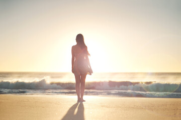 Woman, back and sunset with travel to beach with reflection, relax and vacation by waves. Girl, person and outdoor for peace, wind and summer sunshine at dusk with perspective on holiday by ocean