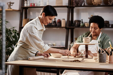 Side view portrait of elegant mature woman creating handmade pottery in art studio lit by sunlight copy space