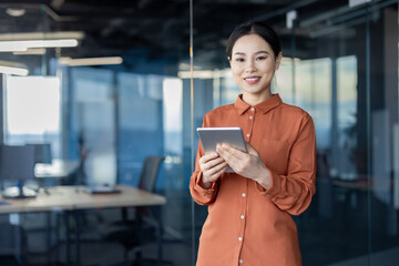 Portrait of a successful Asian female programmer with a tablet computer in her hands, an employee...