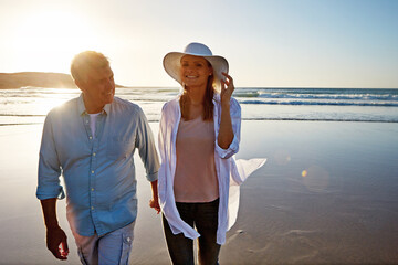 Mature, happy couple and holding hands with beach sunset for love, embrace or bonding together in...