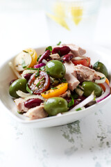 Salad with tuna, green olives and cherry tomatoes. Bright wooden background. Close up. Copy space.