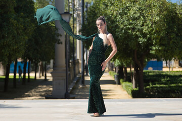 Young, pretty, blonde woman in a green party outfit with sequins, posing as a model while the air blows her cape. Concept of beauty, fashion, trend, model.