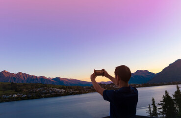 Young tourist man backpack using smartphone take picture at View of landscape sunset  scene in Queenstown ,New zealand