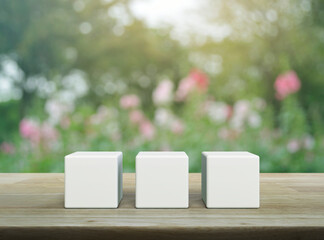 Three white block cubes on wooden table over blur pink flower and tree in garden