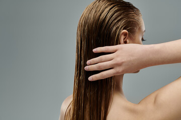 A young woman with long hair is gently touching her wet hair.