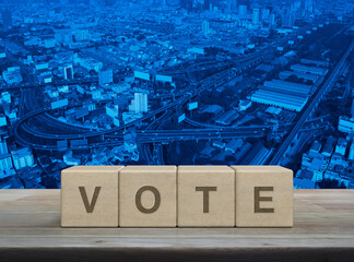 Vote letter on wood block cubes on wooden table over modern city tower, street, expressway and...