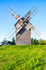A wooden windmill stands tall against a clear blue sky in Borovnice, Czechia. The blades of the windmill are still, and the surrounding countryside is green and lush.