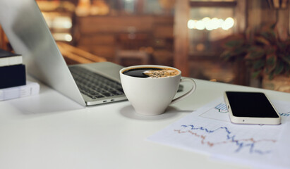Comfortable workplace on table in cafe with black coffee in cup, laptop, and mobile phone with chart