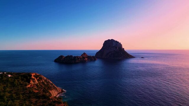 Aerial view of sun setting behind Es Vedra Ibiza during sunset. Showing ocean and clear skies.