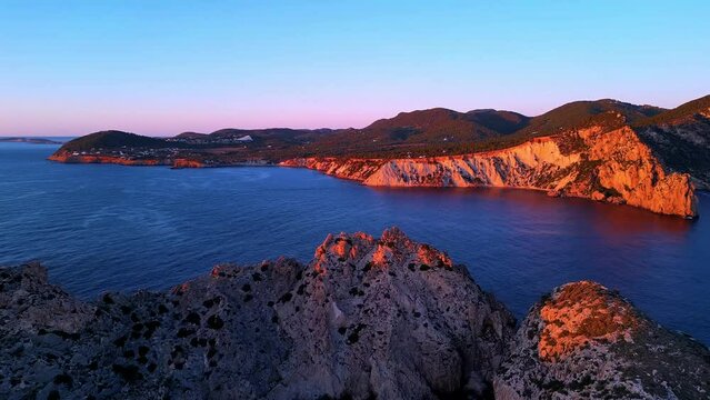 Aerial view of sun setting behind Es Vedra Ibiza during sunset. Showing ocean and clear skies.