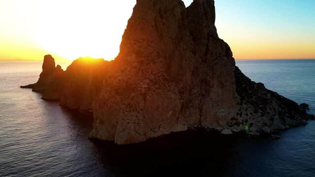Aerial view of sun setting behind Es Vedra Ibiza during sunset. Showing ocean and clear skies.