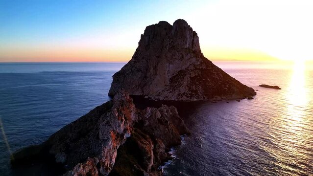 Aerial view of sun setting behind Es Vedra Ibiza during sunset. Showing ocean and clear skies.