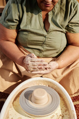 Vertical closeup of senior African American woman enjoying pottery class in sunlight and shaping...
