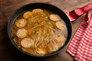 tofu soup mixed with enoki mushrooms. served in a granite skillet on a wooden table. oriental...