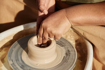 Close up of unrecognizable Black woman creating handmade ceramics on pottery wheel and enjoying art session in sunlight copy space