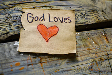 Handwritten "God Loves" Note with Heart on Wooden Surface