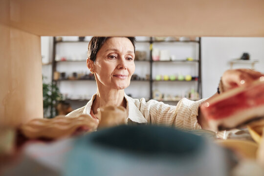POV shot of senior woman putting glazed pottery items in kiln enjoying craft in art studio, copy space