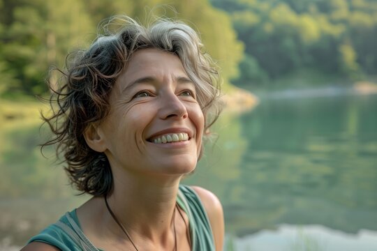 Portrait of a woman in her 50s who exudes happiness and a sense of feeling truly alive in a beautiful natural park near a lake, genuine smile on her face, relaxed and confident, female w