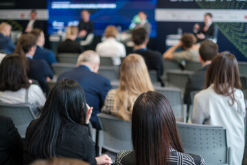 Audience members at a business conference attentively listening to a presentation. The event...