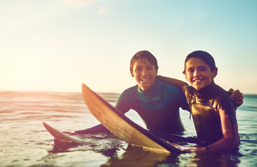 Obraz premium Kids, portrait and happy in water for surfing, sports and wellness with board, blue sky and smile. Excited, boys and swimming at beach as surfer for waves, fitness and summer while on vacation