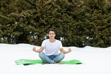 Young handsome man in flight clothing meditating outdoor in the freezing winter day. Healthy lifestyle and preparation for cold concept