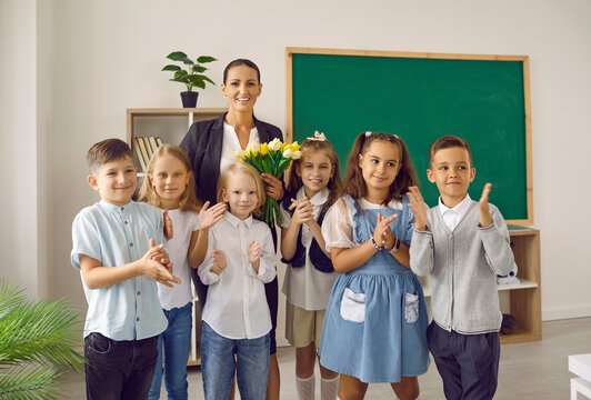 Students make a little surprise for their teacher. Group portrait of happy children and a woman with flowers standing in front of the blackboard in the classroom. Back to school, Teacher's Day concept