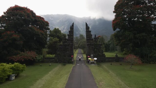 Follow shot of tourists on scooter driving through iconic Handara Gate in Bali, Indonesia