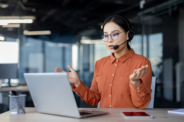 Serious asian woman with headset talking remotely using laptop for video call, help desk worker...