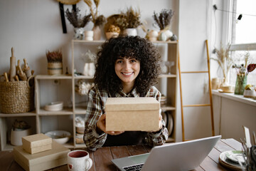 Small business owner packing her handmade product into cardboard box. E-commerce entrepreneurship. Female online store preparing an order for shipping in a warehouse.