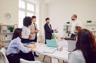 Young confident business man talking about company growth and finance discussing job project on meeting. People employees sitting in modern office with colleagues on work conference. Teamwork concept